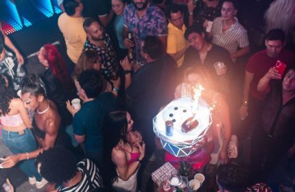 Crowded dance floor at The Back Door gay bar in Cancun. Waitress carries a tray with a flaming dessert. Gay nightlife travel.