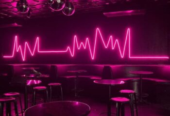 Interior of The Back Door Gay Bar in Cancun, Mexico. Pink neon heartbeat sign, disco balls, tables, and stools. Nightlife for gay men.