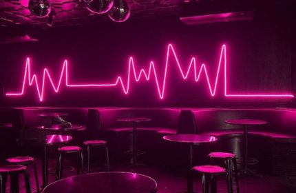Interior of The Back Door Gay Bar in Cancun, Mexico. Pink neon heartbeat sign, disco balls, tables, and stools. Nightlife for gay men.