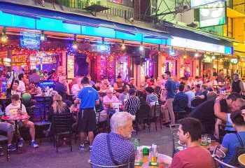 The Balcony Pub Bangkok gay bar open early hours in Silom. Outdoor seating area filled with people at tables and bar. Nightlife scene.
