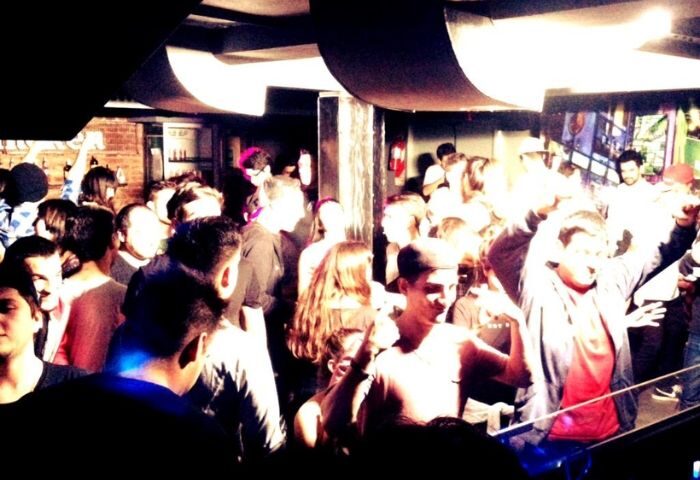 The Basement Club, Barcelona. A packed gay cruise club with a diverse crowd, enjoying music and dancing in a dimly lit, energetic atmosphere.