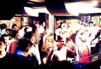 The Basement Club, Barcelona. A packed gay cruise club with a diverse crowd, enjoying music and dancing in a dimly lit, energetic atmosphere.