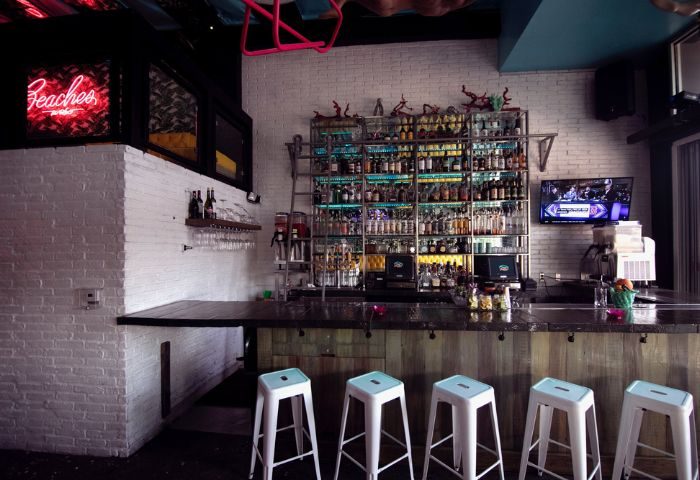 Beaches WeHo: Interior of The Bayou Bar. Well-stocked bar with stools, brick walls, neon sign, and TV. Gay bar in West Hollywood.