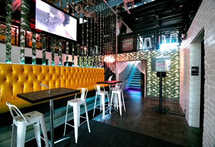 Beaches WeHo: The Bayou Experience interior. Yellow booth seating, tables, bar stools, mirrored walls, and stairs. Gay bar travel advice.