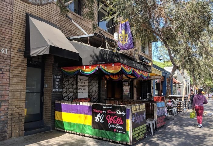 The Bayou location: Gay bar exterior with rainbow flags and a fleur-de-lis banner. Happy hour specials advertised. A gay travel destination.