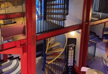 Interior view of The Boilerhouse gay sauna in Dublin. Red beams, spiral staircase, and elevator panel are visible. Gay travel.