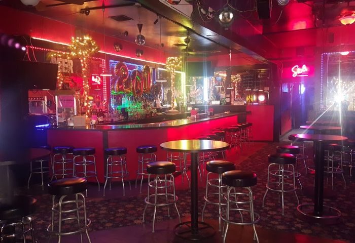 Interior of The Boulevard Bar location. Red lighting, bar stools, and tables. Gay bar with a festive atmosphere. Perfect for gay travel.