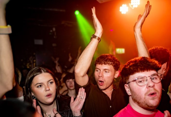 Enthusiastic crowd at The Brewers Manchester, a gay bar. People with hands raised, enjoying the vibrant nightlife scene. Gay travel advice.
