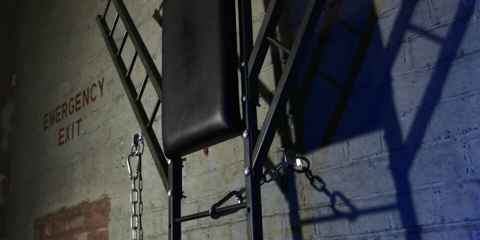 The Bunker London's private appointment only gay cruise club. Interior shot of a dungeon with chains and emergency exit sign.