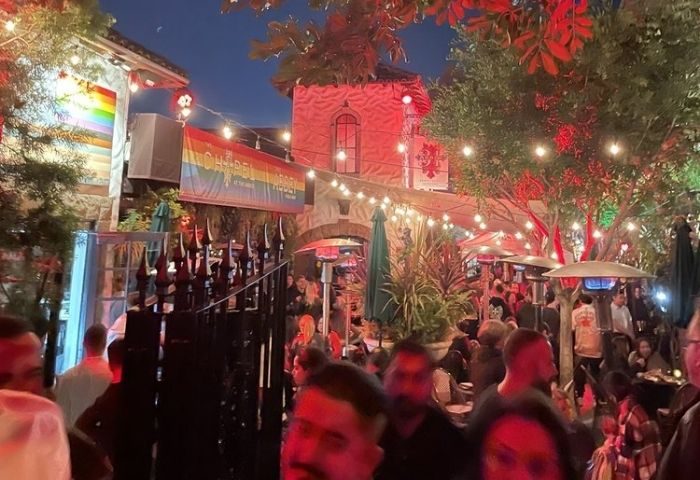 Night out at The Chapel @ The Abbey, a gay bar. Rainbow flag, string lights, and a crowd of people enjoying the outdoor space. Gay travel.