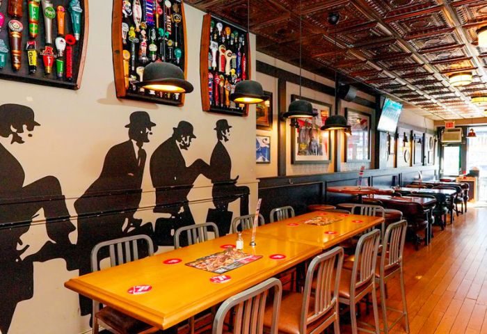 Interior of The Church Mouse Pub in Toronto. Silhouettes of men adorn the wall, bowler hat lamps hang above tables. Gay travel.