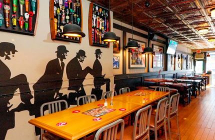 Interior of The Church Mouse Pub in Toronto. Silhouettes of men adorn the wall, bowler hat lamps hang above tables. Gay travel.