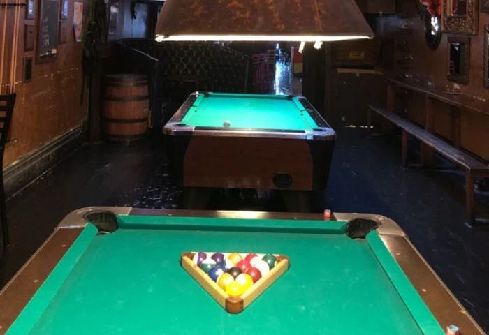 Interior of The Cinch Saloon, a gay bar in San Francisco. Pool tables, bar stools, and a barrel are visible, creating a classic saloon vibe.