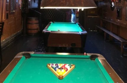 Interior of The Cinch Saloon, a gay bar in San Francisco. Pool tables, bar stools, and a barrel are visible, creating a classic saloon vibe.