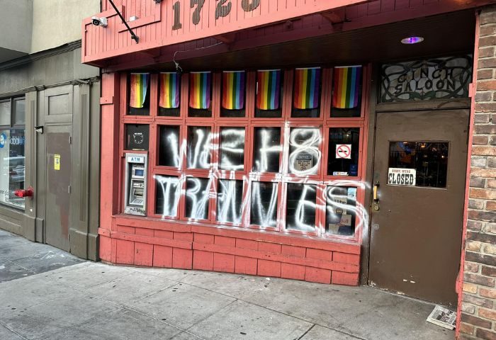 The Cinch Saloon in San Francisco, a gay bar, vandalized with graffiti. Rainbow flags hang above the windows. The door is closed.