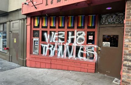 The Cinch Saloon in San Francisco, a gay bar, vandalized with graffiti. Rainbow flags hang above the windows. The door is closed.