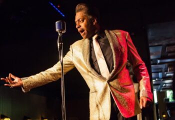 Drag show at The Cock Tavern, a cool gay bar in London. Performer in a gold jacket sings into a microphone on stage. LGBTQ+ nightlife.