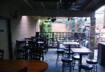 Outdoor patio at The Crest, a gay-friendly location. Tables, chairs, and bar stools are arranged for socializing and enjoying the ambiance.