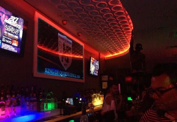 The Deep End Resto-Bar in New York. Gay bar with red lighting, TVs, and a sign reading King of Queens. Gay travel destination.
