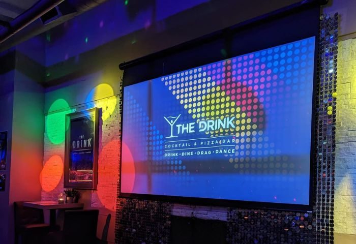 The Drink Cocktail Pizza Bar in Toronto, a gay-friendly bar. Screen shows the bar's logo with Drink, Dine, Drag, Dance. Disco lights.