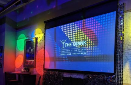 The Drink Cocktail Pizza Bar in Toronto, a gay-friendly bar. Screen shows the bar's logo with Drink, Dine, Drag, Dance. Disco lights.