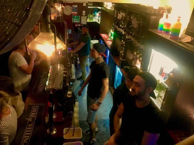 Inside The Duke of Wellington gay bar in London. Men at the bar with rainbow bottles. Gay travel advice in London.