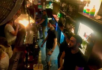Inside The Duke of Wellington gay bar in London. Men at the bar with rainbow bottles. Gay travel advice in London.