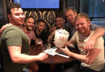 Gay men at Duke of Wellington gay bar, London. Group of friends enjoying drinks, socializing, and having fun in a London gay bar.
