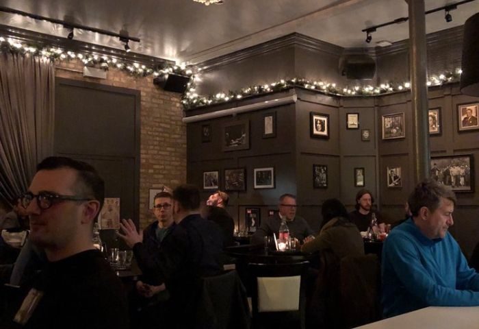 Interior of The Elixir Lounge, a gay bar in Chicago. People are seated at tables, with string lights decorating the walls.