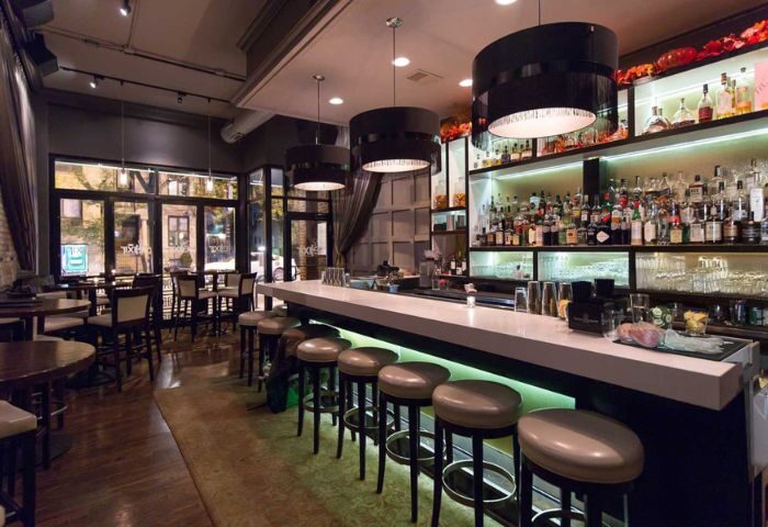 Interior of The Elixir Lounge, a gay bar in Chicago. Bar stools line the bar, with liquor bottles displayed on shelves behind.