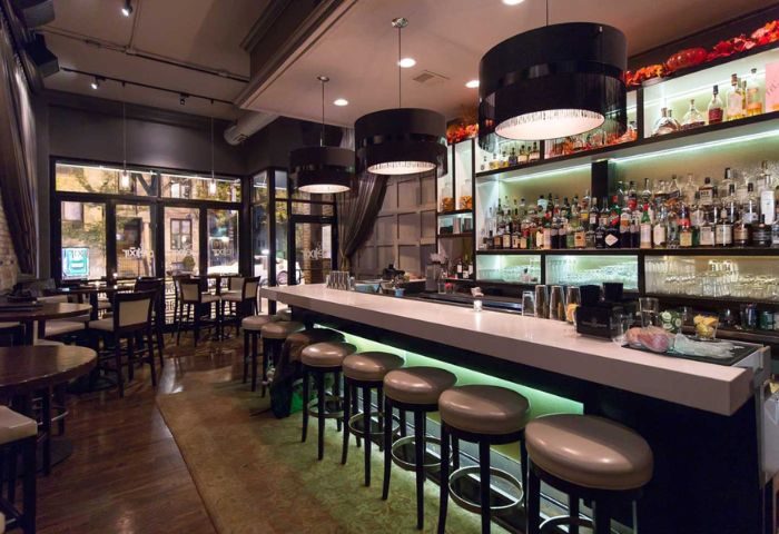 Interior of The Elixir Lounge, a gay bar in Chicago. Bar stools line the bar, with liquor bottles displayed on shelves behind.