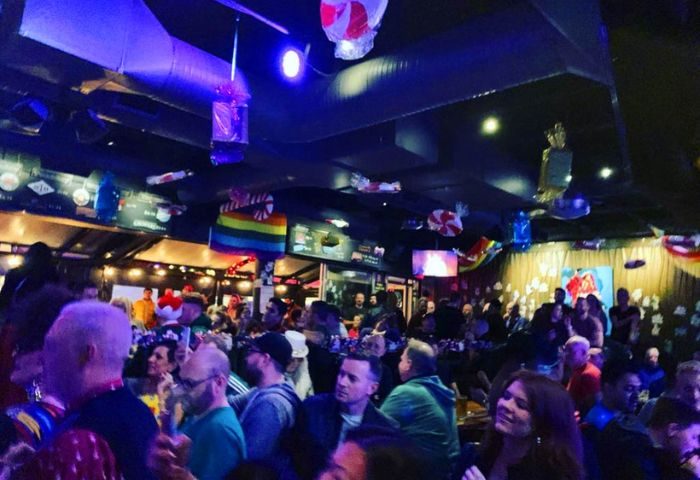 Crowded interior of The Fountainhead Pub in Vancouver. Gay bar with rainbow flags, people mingling, and a vibrant atmosphere. Gay travel advice.