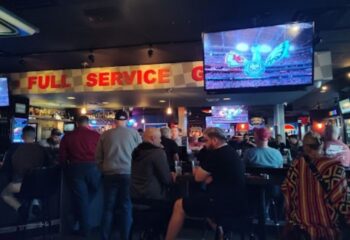 Gay bar, The Garage, in Las Vegas. Men watch a game on TV at the bar. Full service sign. Gay travel advice for Vegas.