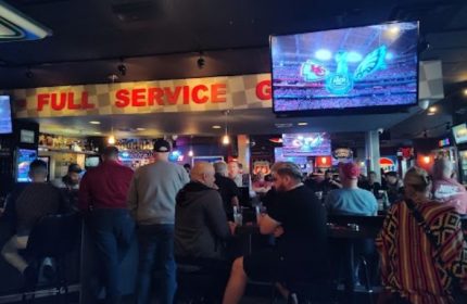 Gay bar, The Garage, in Las Vegas. Men watch a game on TV at the bar. Full service sign. Gay travel advice for Vegas.