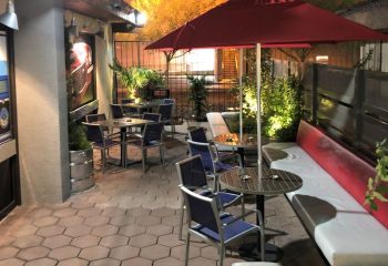 The Garage in Las Vegas outdoor patio. Tables, chairs, and a red umbrella offer a relaxed vibe. A gay-friendly spot for drinks & socializing.