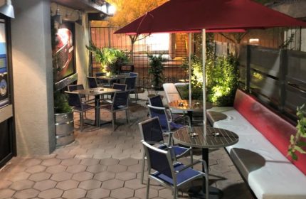 The Garage in Las Vegas outdoor patio. Tables, chairs, and a red umbrella offer a relaxed vibe. A gay-friendly spot for drinks & socializing.