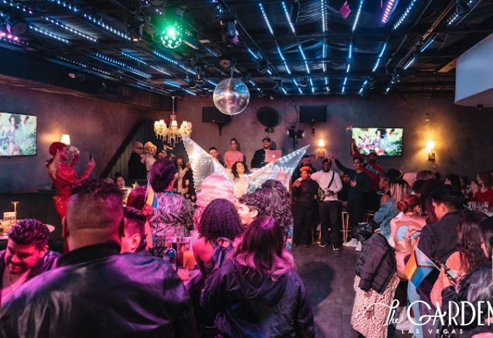 The Garden Las Vegas gay bar interior. Drag queen performing for a crowd. Disco ball, stage lights, and bar patrons. Gay nightlife travel.