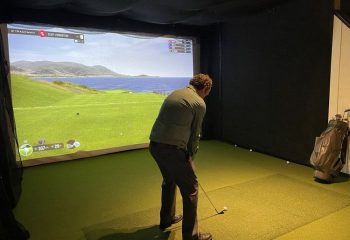 Man plays virtual golf at The Glenwood gay bar in Chicago. Indoor simulator shows a seaside course. Gay travel advice.