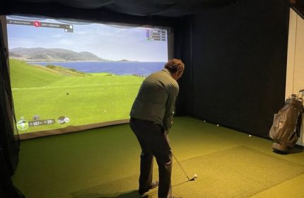 Man plays virtual golf at The Glenwood gay bar in Chicago. Indoor simulator shows a seaside course. Gay travel advice.