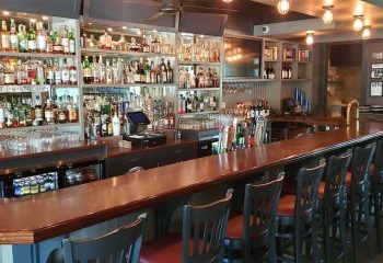 Interior view of The Glenwood gay bar in Chicago. Bar stools line the counter, liquor bottles fill shelves behind the bar.