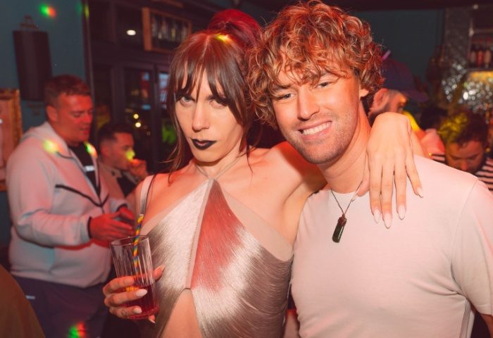 Two people at The Goose Manchester, a gay bar. One holds a drink with a rainbow straw. Gay travel advice, nightlife.