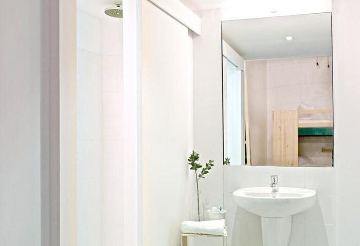 Bathroom at The Hat Hostel Madrid, a top gay hostel near Gran Via. Features a shower, sink, mirror, and minimalist decor. Ideal for gay couples.