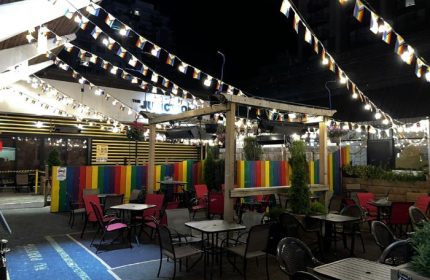 The Junction Pub in Vancouver at night. Outdoor seating area with rainbow flags and colorful decor. Gay bar travel destination.