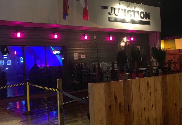 The Junction Pub in Vancouver. Exterior view of the gay bar with pink lights, flags, and a wooden fence. Nightlife for gay men travel.