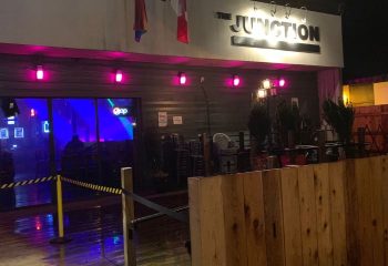 The Junction Pub in Vancouver. Exterior view of the gay bar with pink lights, flags, and a wooden fence. Nightlife for gay men travel.