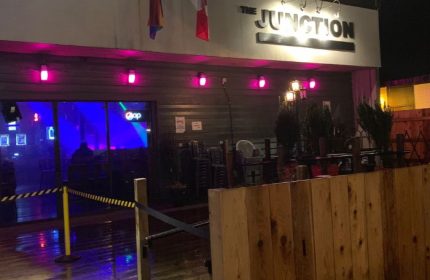 The Junction Pub in Vancouver. Exterior view of the gay bar with pink lights, flags, and a wooden fence. Nightlife for gay men travel.