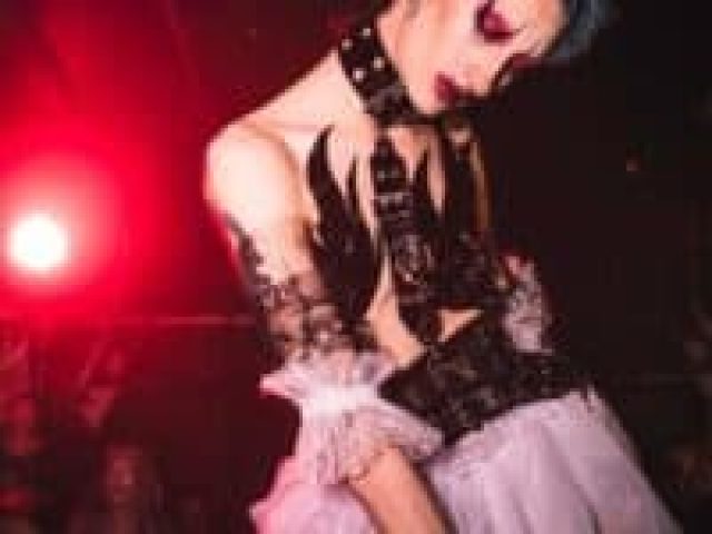 Drag queen at The Karaoke Hole gay bar. Performer in edgy costume with red lighting. Gay travel nightlife in London.