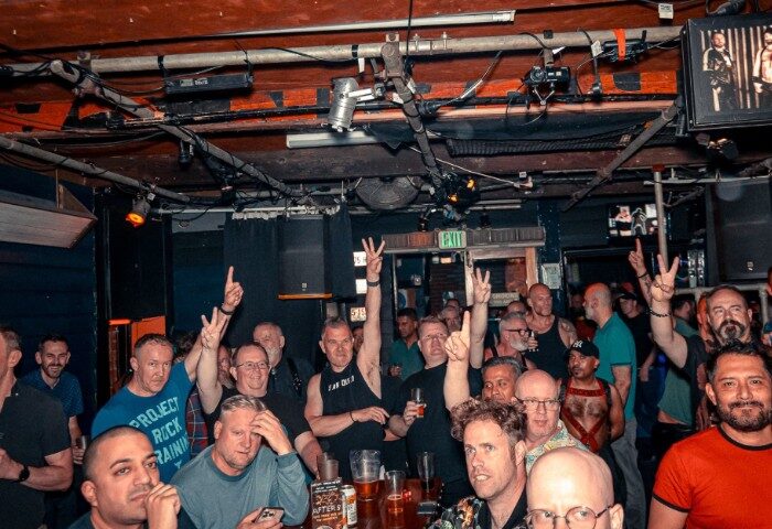 The Laird Melbourne: A lively crowd of gay men at a bar, many raising hands. Gay travel advice in Melbourne, Australia.