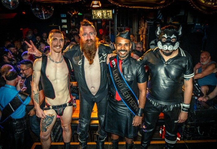 The Laird Melbourne event: four gay men in leather gear, one in a puppy mask, posing at a gay bar. Leather and fetish scene.
