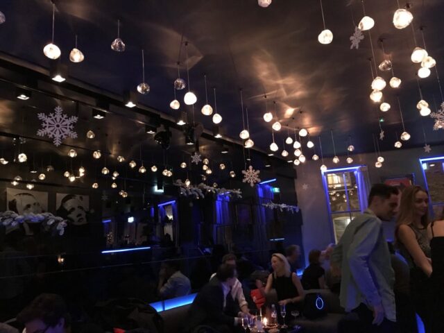Interior of The Light Lounge gay bar. Festive lighting, snowflakes, and people socializing in a stylish, dimly lit space.